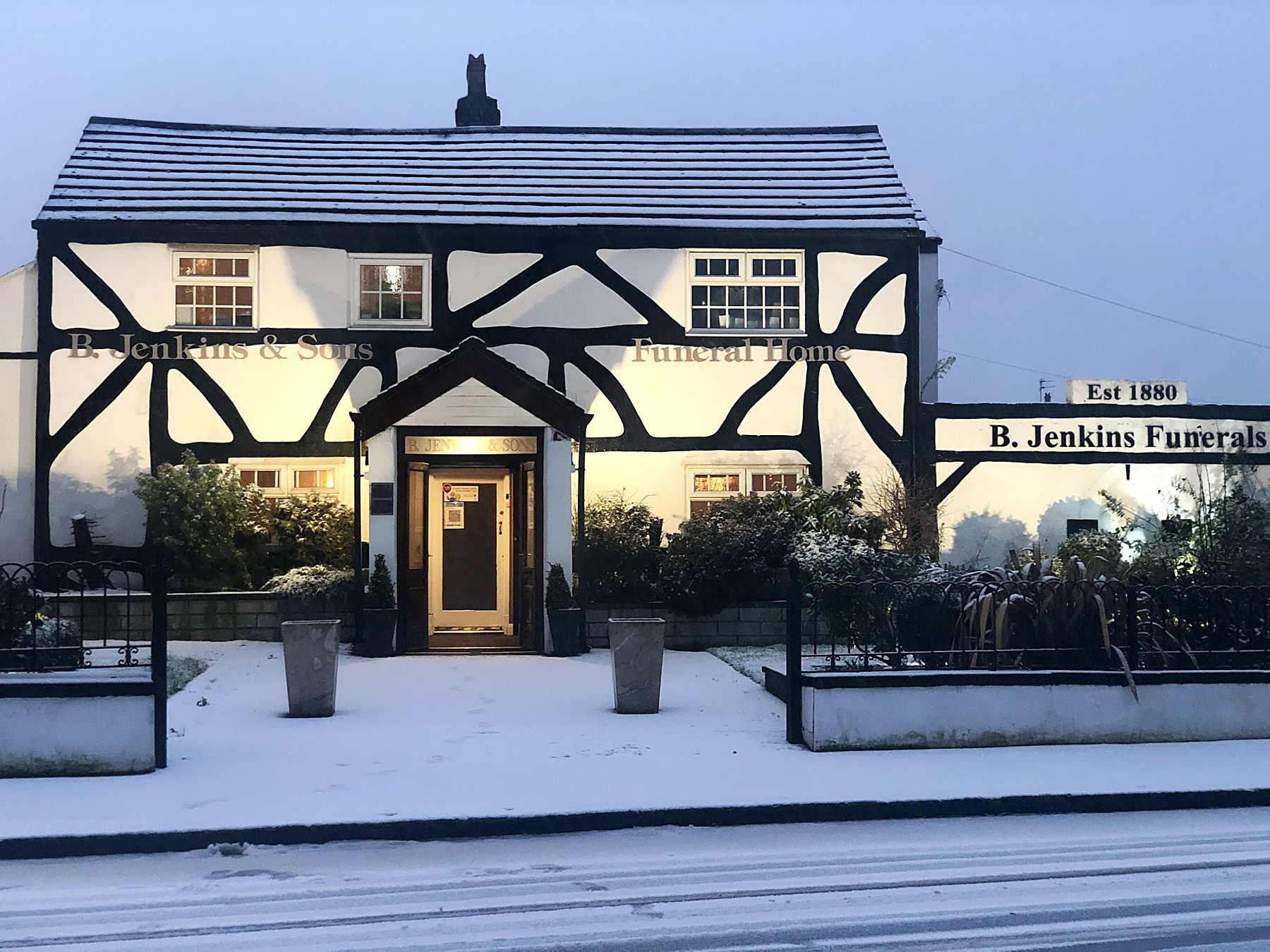 The Tudor cottage funeral home lit at dusk after snow