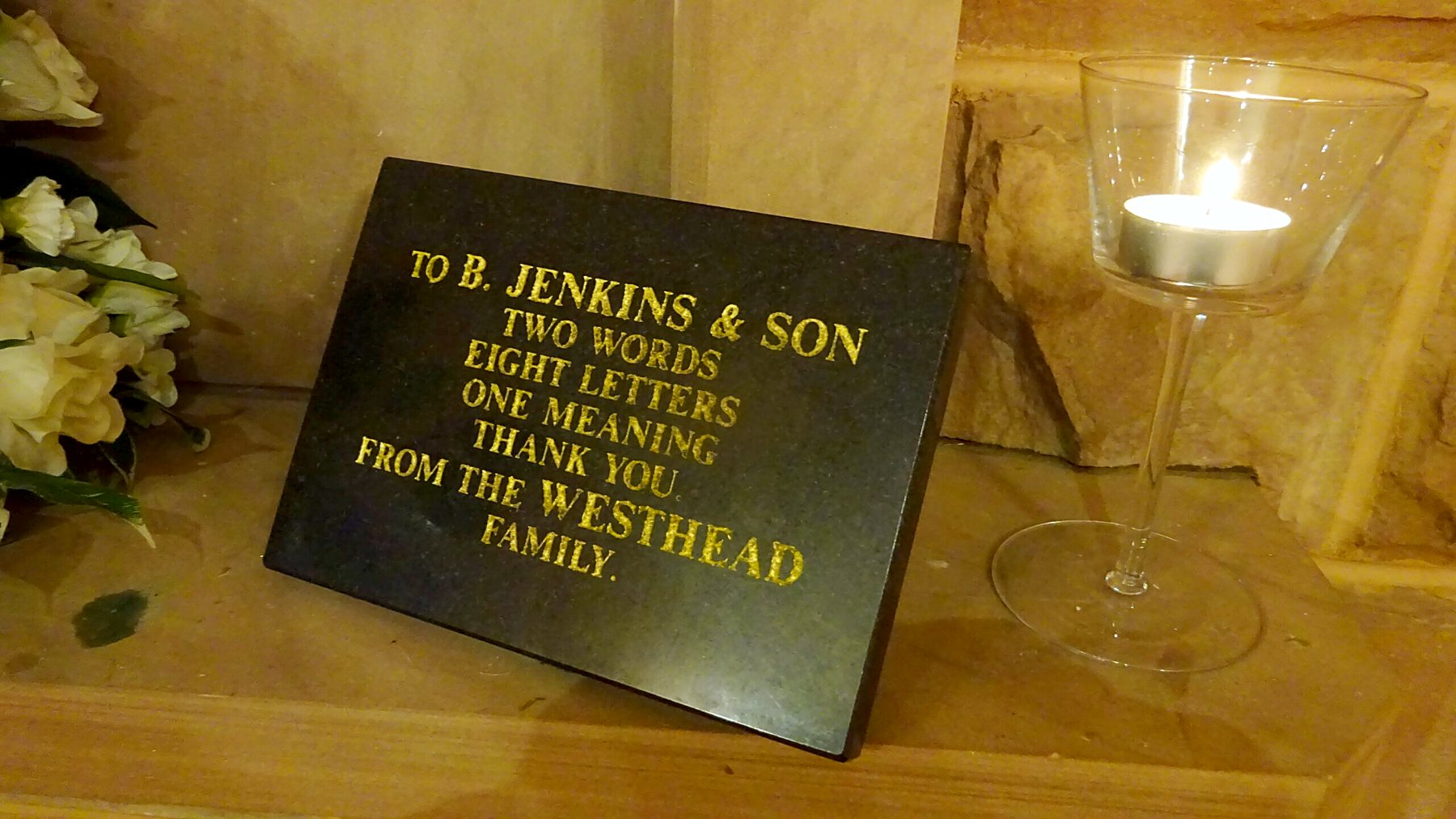 An engraved granite plaque left in the chapel by a family, reading two words, eight letters, one meaning, thank you